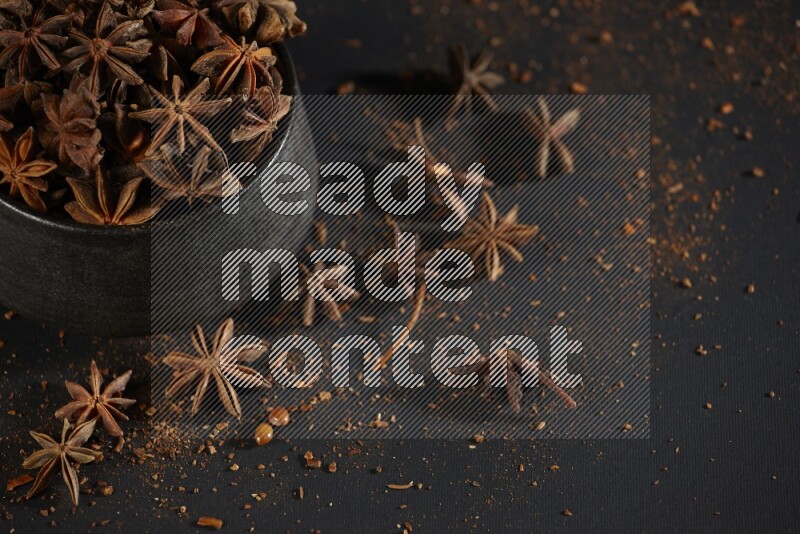 Star Anise in a black bowl with sprinkled anise on black flooring