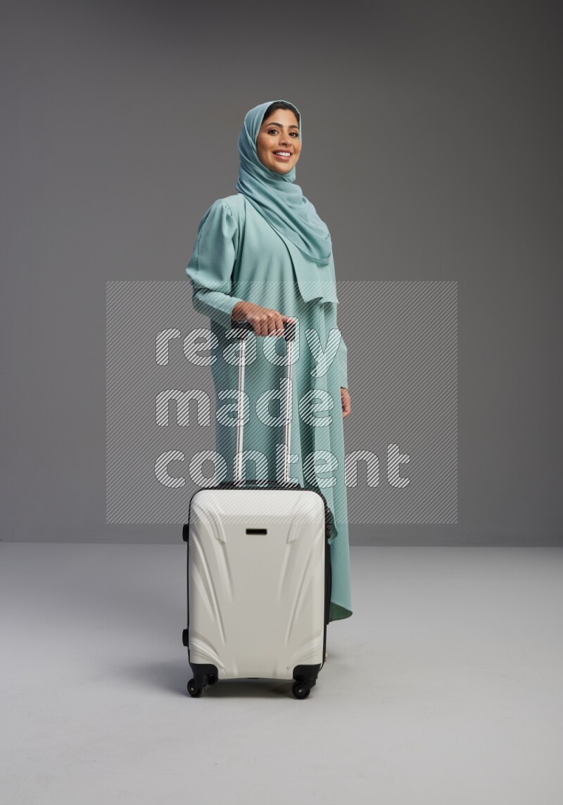 Saudi Woman wearing Abaya standing holding Travel bag on Gray background