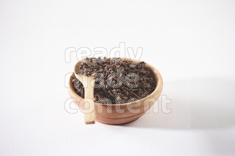 A wooden bowl and a wooden spoon full of cloves on a white flooring