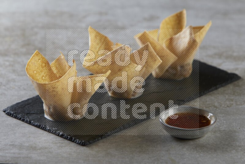 wonton cups with soy sauce ramkin on rectangle slate on grey textured counter top