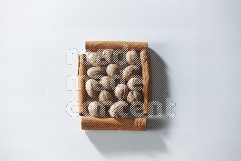 أربعة من أعواد القرفة مكونة شكل مربع بداخلها جوزة الطيب علي خلفية بيضاء