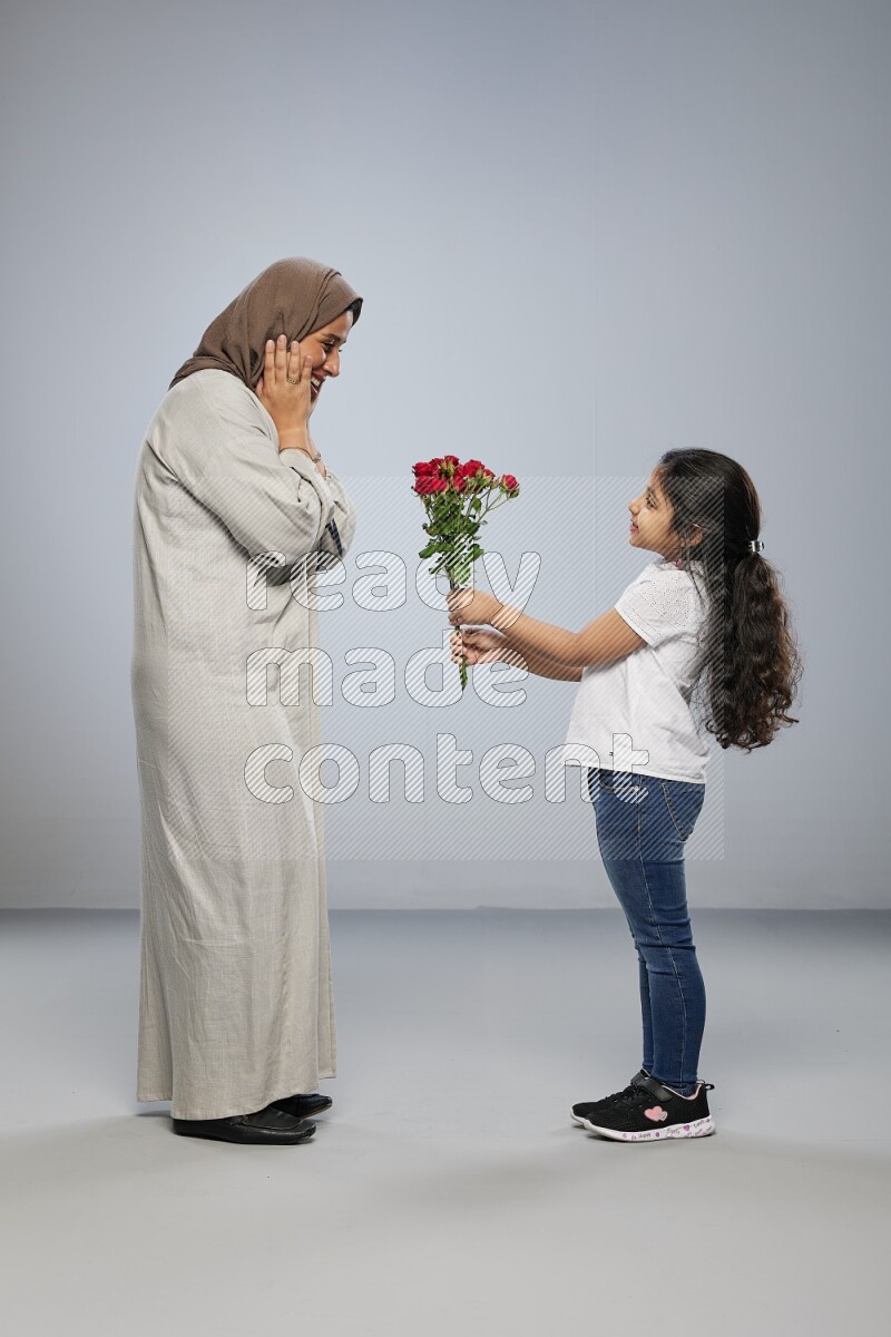 A girl standing giving flowers to her mother on gray background