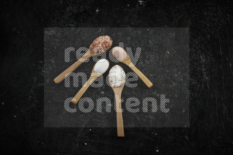 4 wooden spoons filled with fine and coarse salt on black background