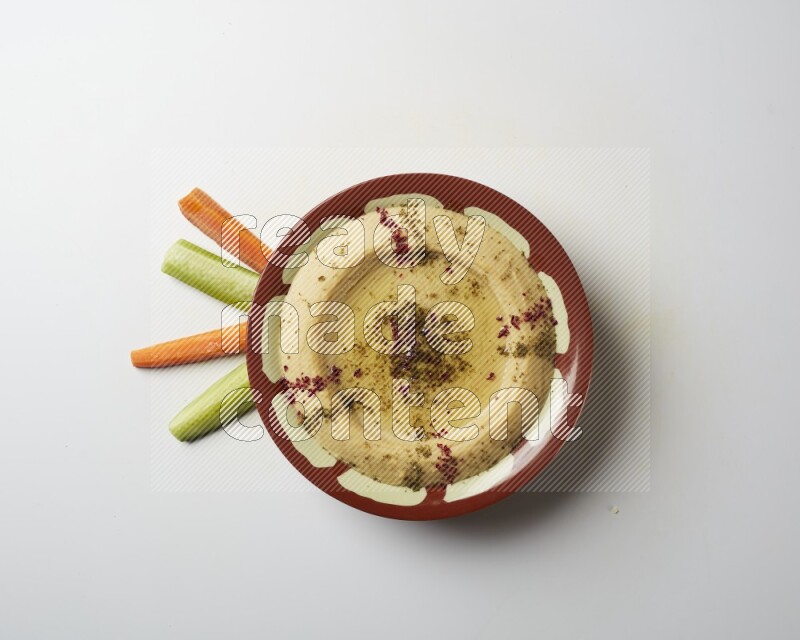 Hummus in a traditional plate garnished with zaatar & sumak on a white background