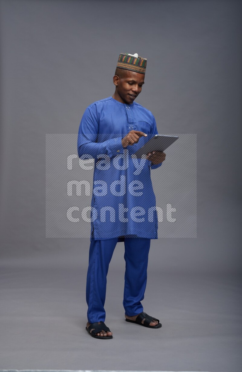 Man wearing Nigerian outfit standing working on tablet on gray background