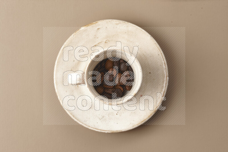 A beige pottery cup full of roasted coffee beans on beige background
