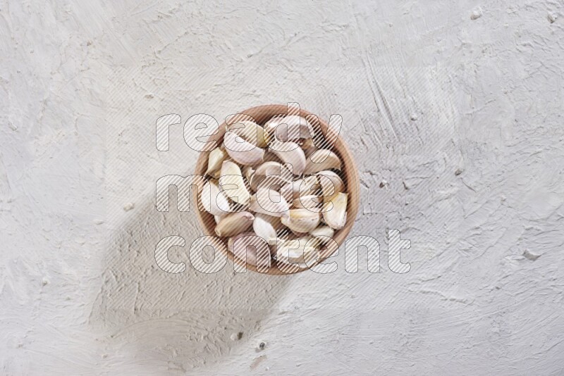 A wooden bowl full of garlic cloves on a white flooring