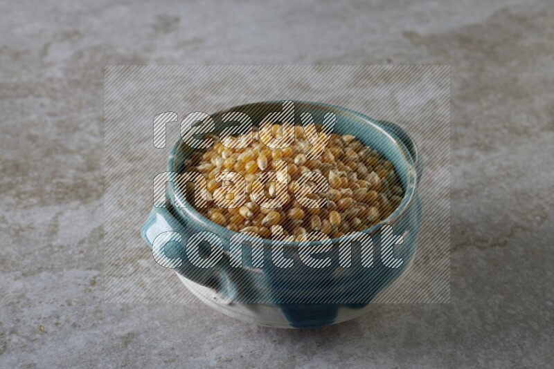 corn kernel in a multi-colored handheld ceramic bowl on a grey textured countertop