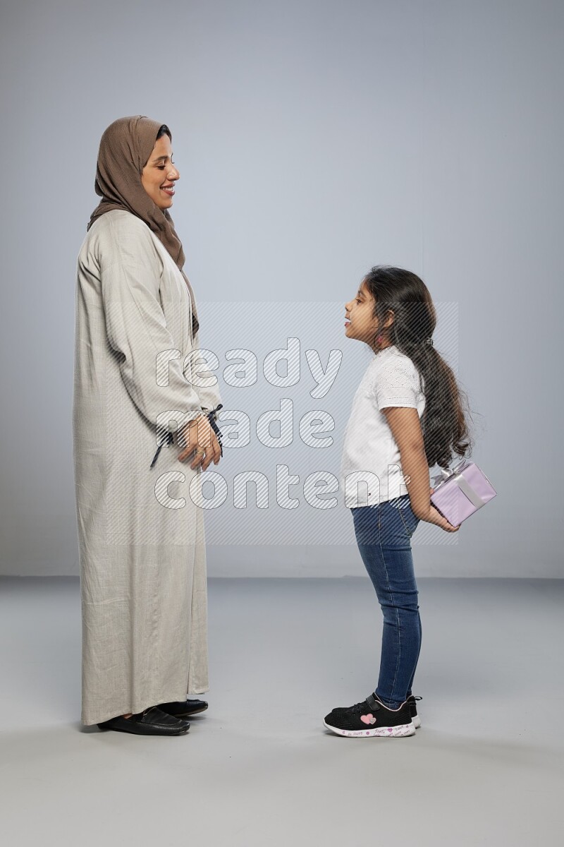 A girl standing hiding a gift behind her back for her mother on gray background