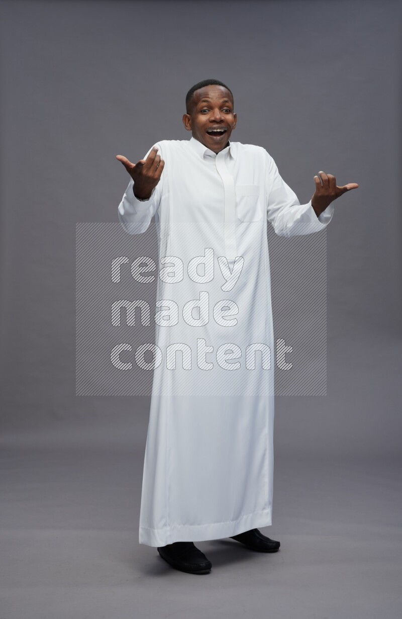 Saudi man wearing thob standing interacting with the camera on gray background