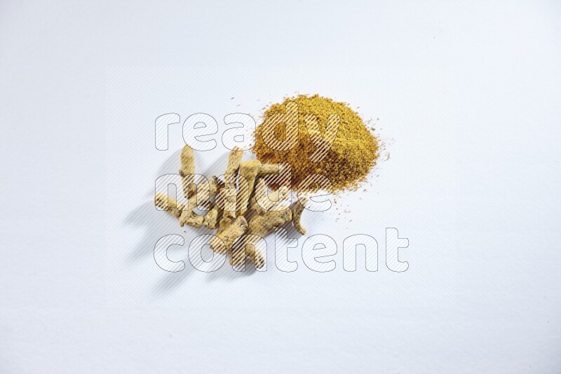 Turmeric powder and dried turmeric whole fingers on white flooring