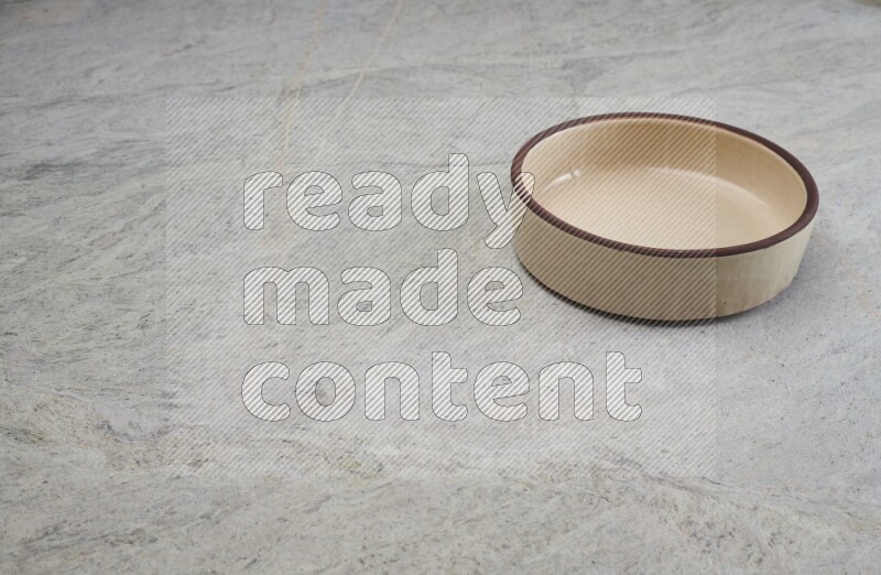 A beige pottery oven bowl on grey marble background