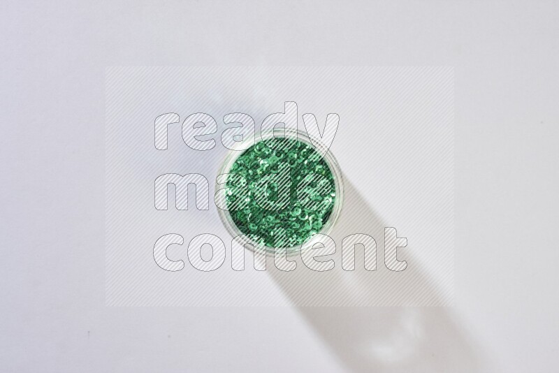 Colored flat sequins in a glass jar on grey background