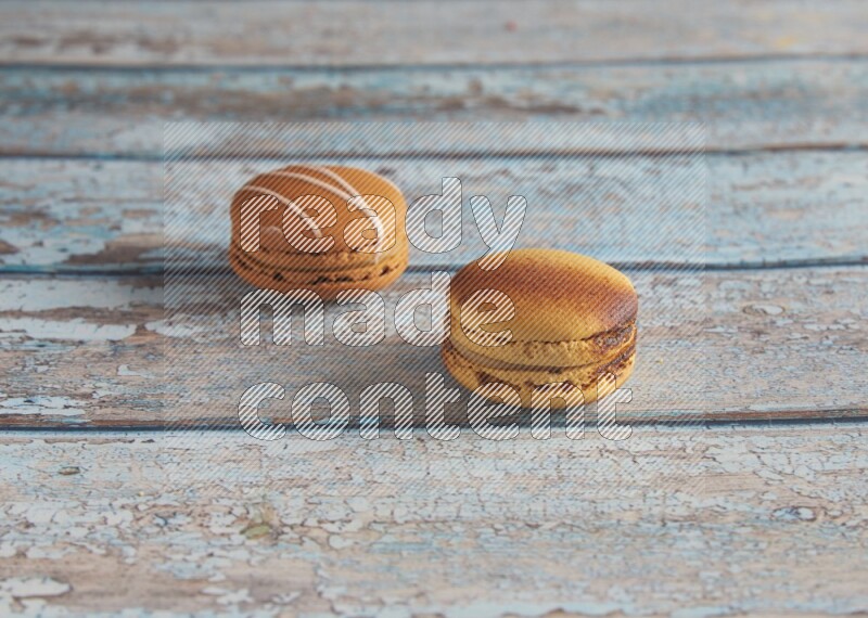 45º Shot of of two assorted Brown Irish Cream, and Yellow Crème Brulée macarons on light blue background