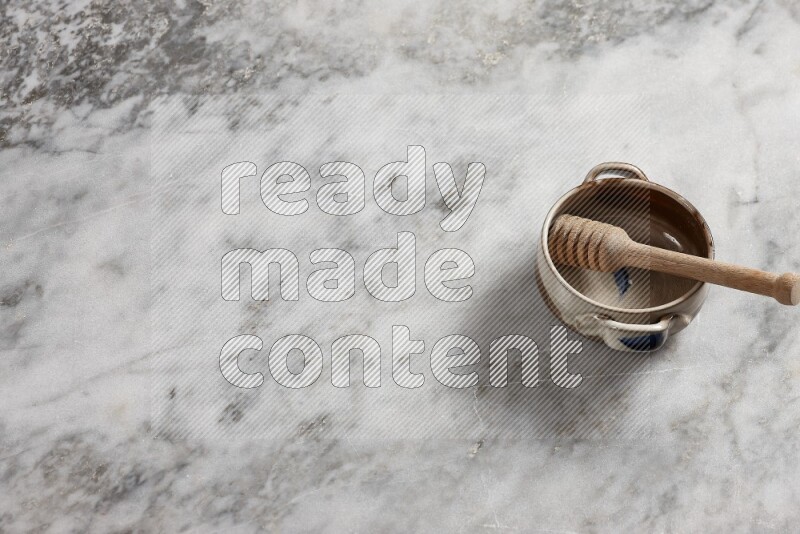 وعاء فخاري متعدد الألوان مع ملعقة عسل خشبية بداخله على خلفية من الرخام الرمادي