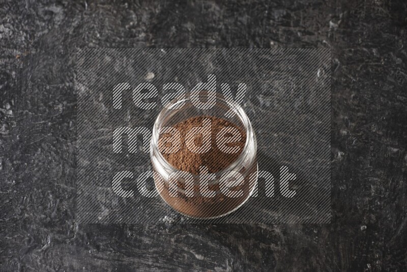 A glass jar full of cloves powder on a textured black flooring