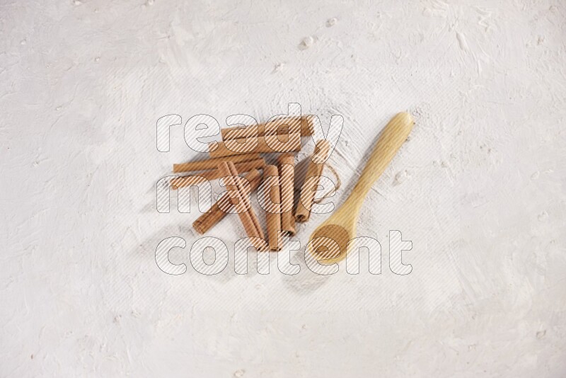 Cinnamon sticks stacked beside a wooden spoon full of cinnamon powder on white background