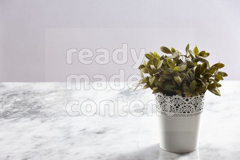 Green artificial plant in white decorative pot on grey marble background