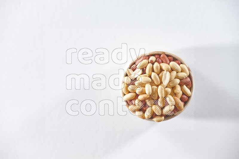 A beige ceramic bowl full of peeled peanuts on a white background in different angles