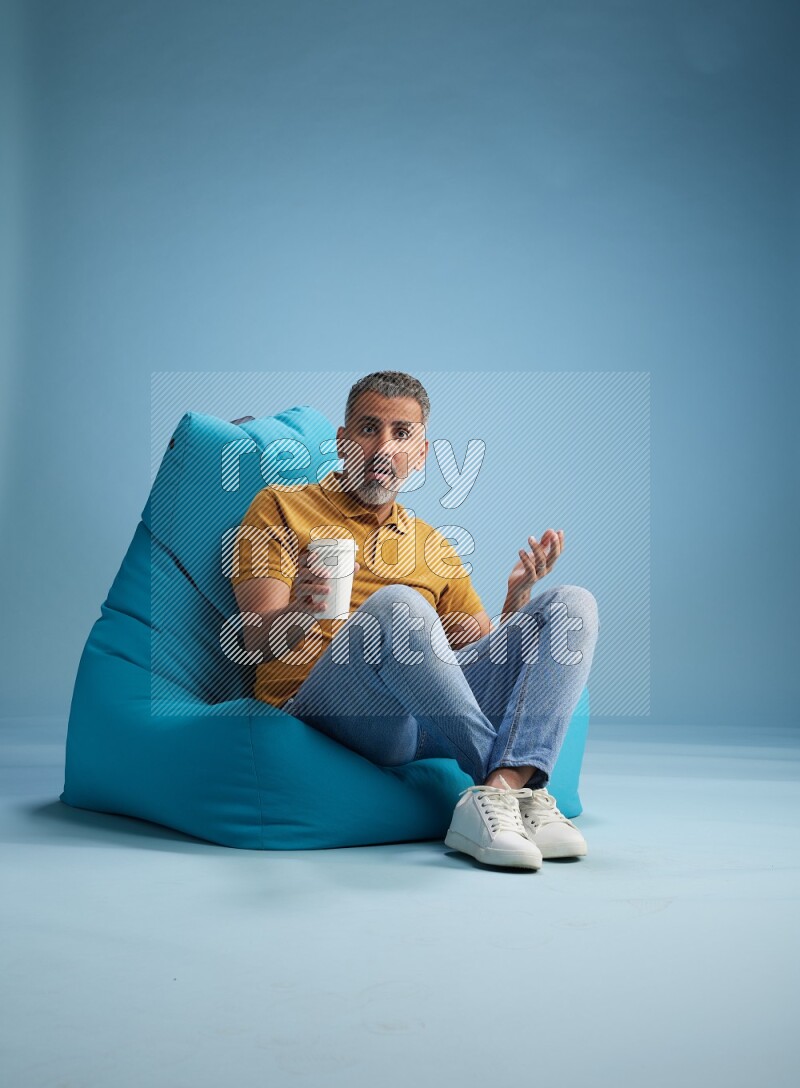 A man sitting on a blue beanbag and drinking coffee
