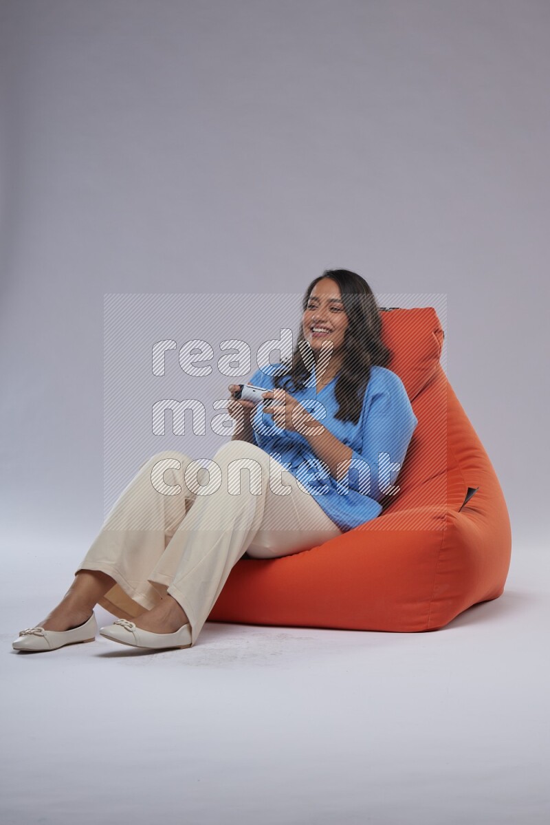 A woman sitting on an orange beanbag and gaming with joystick