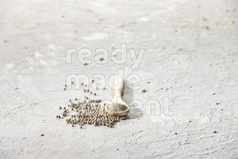 A wooden spoon full of white pepper powder and white pepper beads on textured white flooring