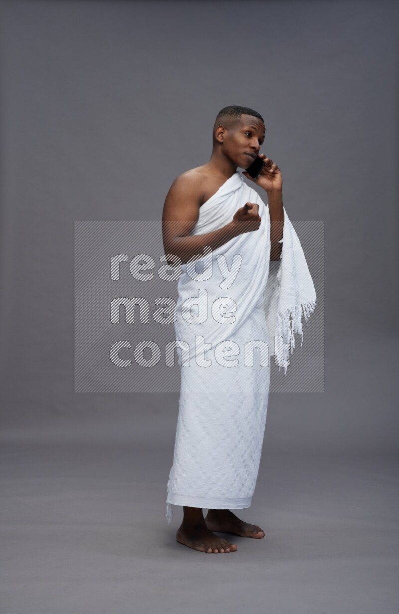 A man wearing Ehram Standing talking on phone on gray background