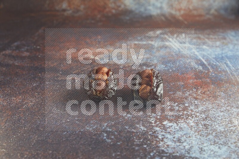 two hazelnut stuffed madjoul dates on a rustic reddish background