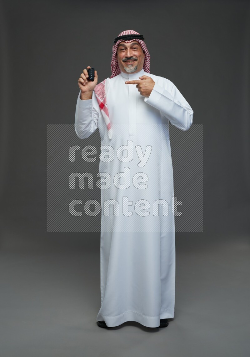 Saudi man with shomag Standing holding car key on gray background