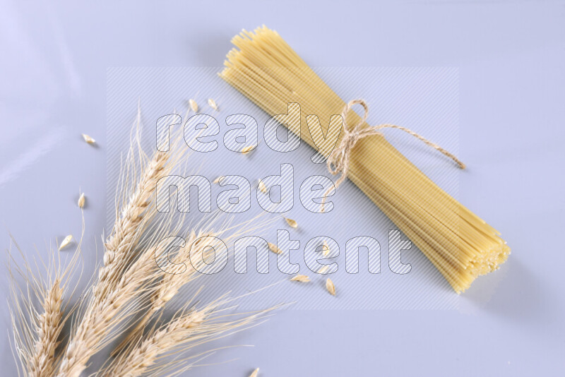 Raw pasta with wheat stalks on light blue background
