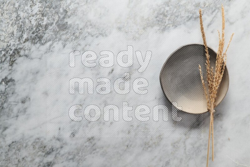 Wheat stalks on multicolored pottery plate on grey marble background