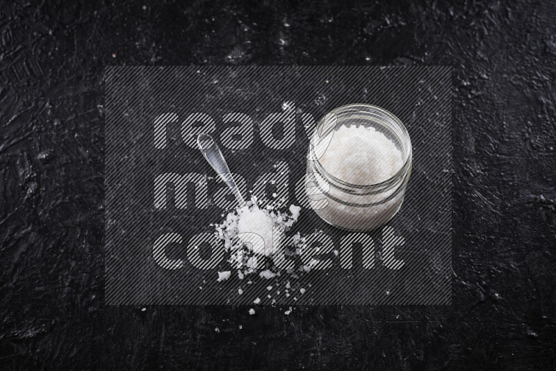 A glass jar full of coarse sea salt crystals on black background
