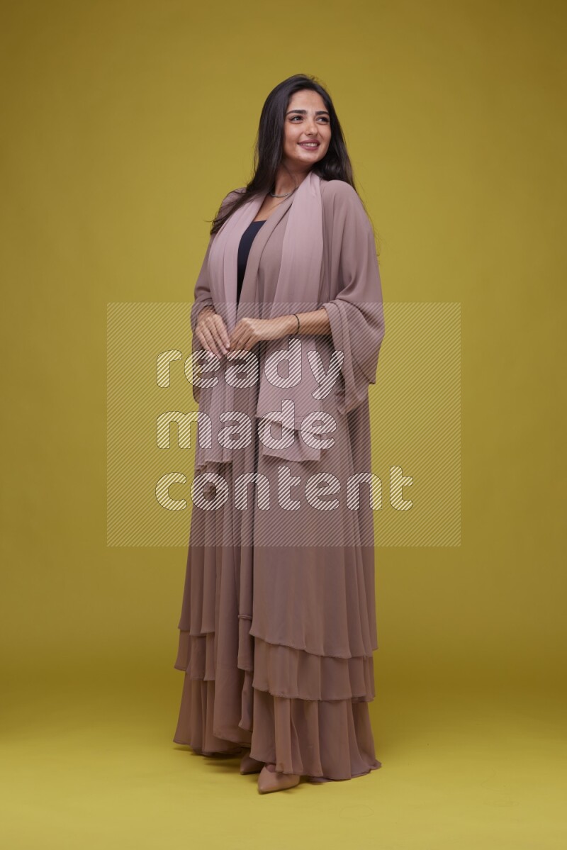A woman Posing on a Yellow Background wearing Brown Abaya