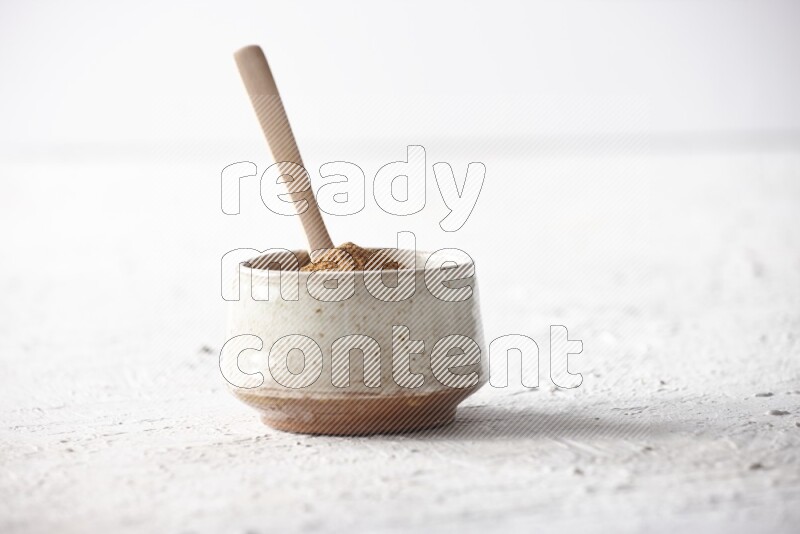 Ceramic beige bowl full of cinnamon powder with a wooden spoon on a textured white background