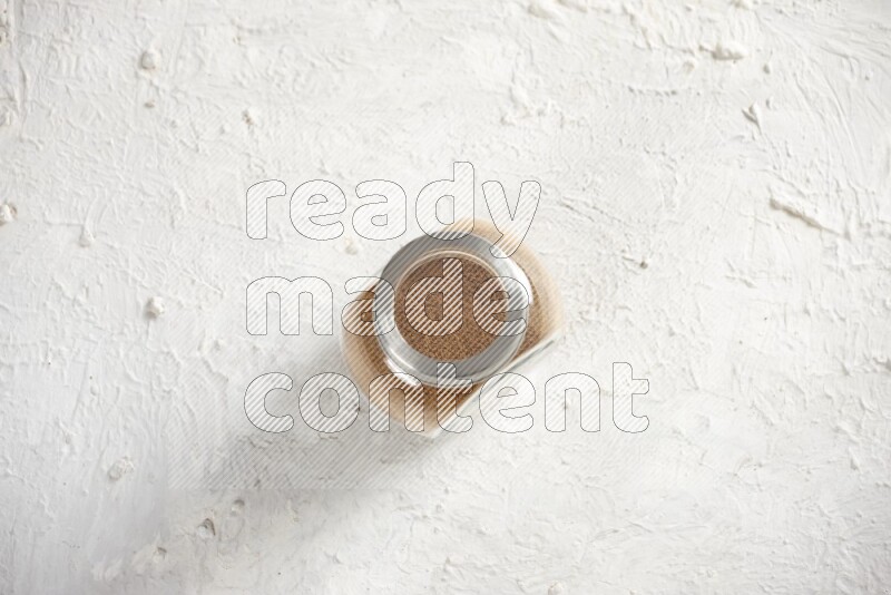 Herbs glass jar full of cinnamon powder on a textured white background