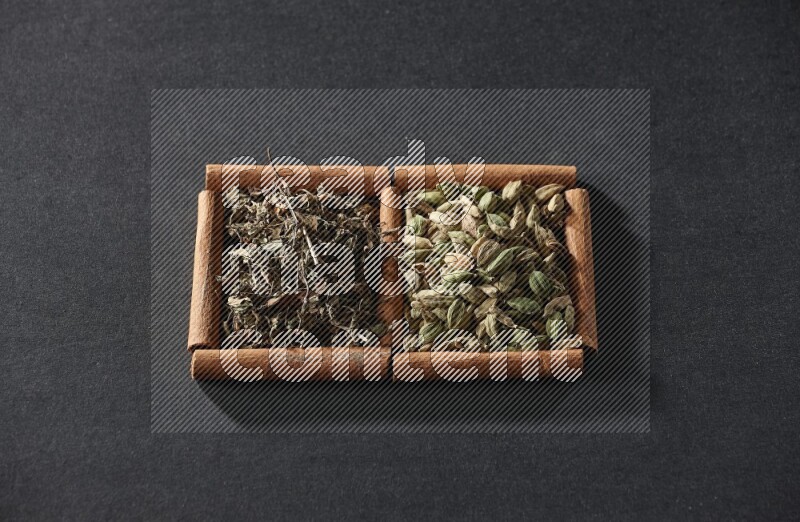 مربعان من أعواد القرفة ممتلئان بحبوب الهيل والريحان المجفف علي خلفية سوداء