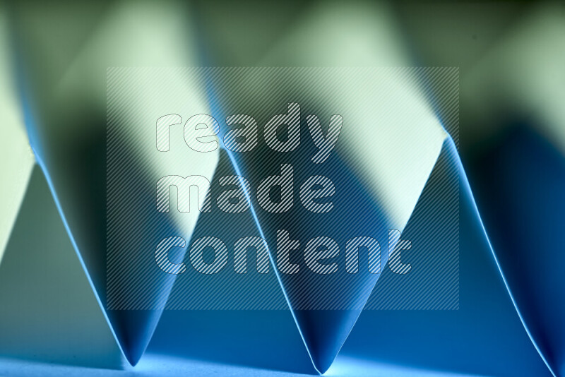 A close-up abstract image showing sharp geometric paper folds in green and blue gradients