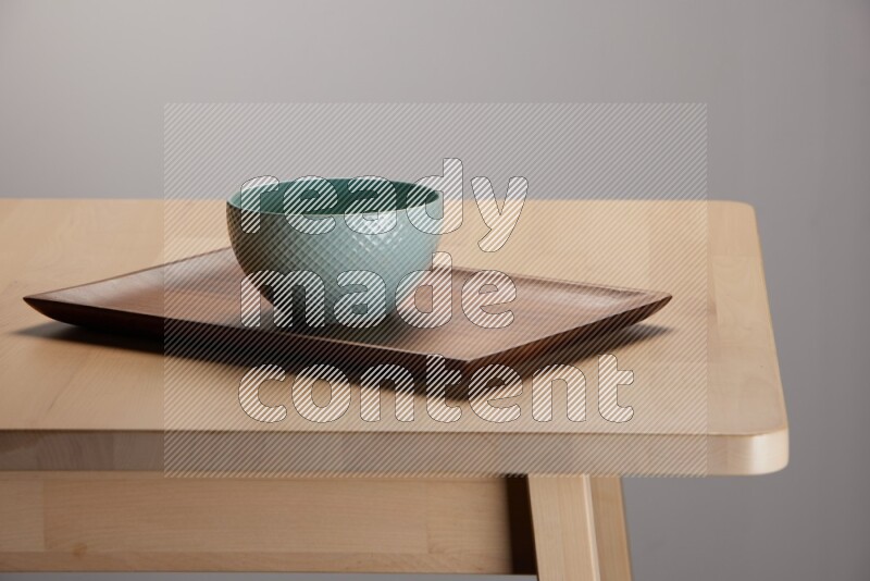 blue bowl placed on a rectangular wooden tray on the edge of wooden table