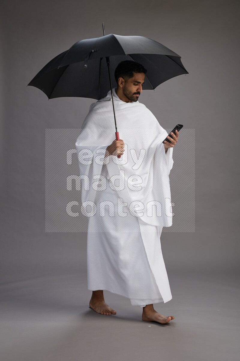 A man wearing Ehram Standing holding umbrella on gray background