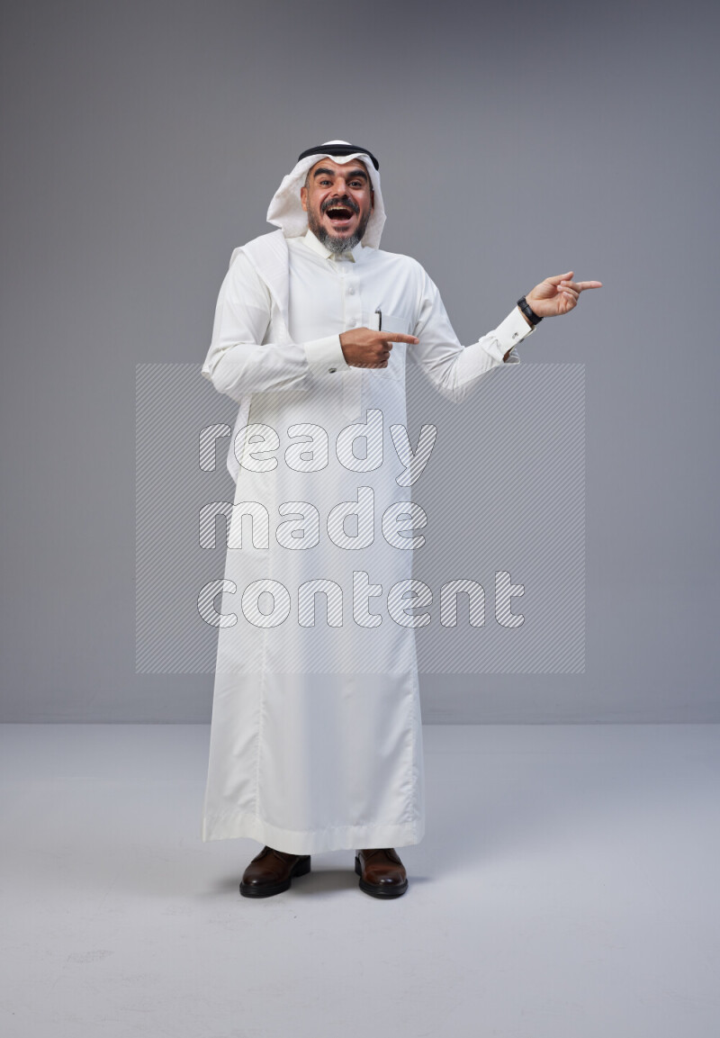 Saudi man Wearing Thob and white Shomag standing interacting with the camera on Gray background