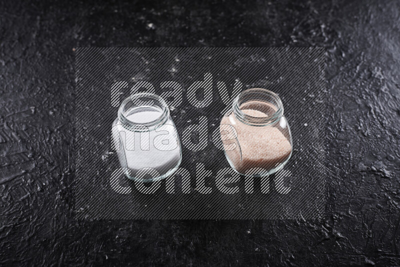 2 glass jars one is filled with fine himalayan salt and the other with table salt on black background