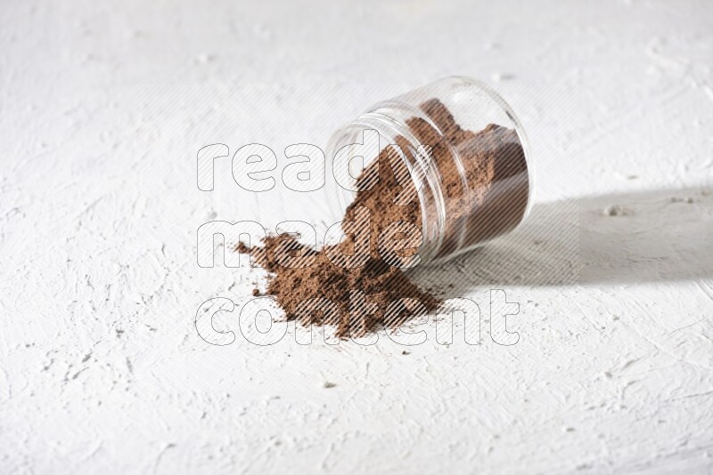 A flipped glass jar full of cloves powder on a textured white flooring