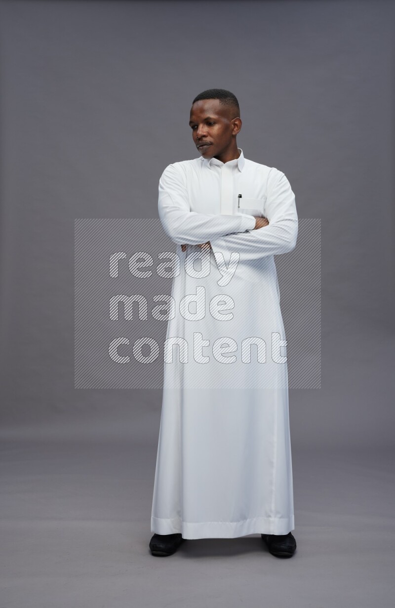 Saudi man wearing thob standing with crossed arms on gray background