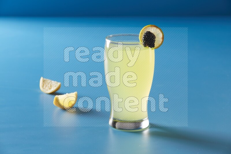 glass of lemon juice with lemon slice and berry on blue background