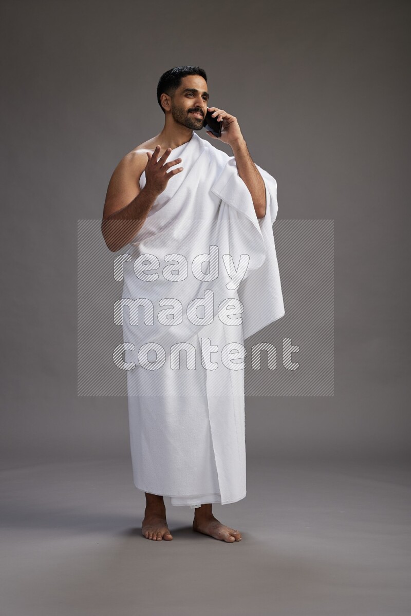 A man wearing Ehram Standing talking on phone on gray background