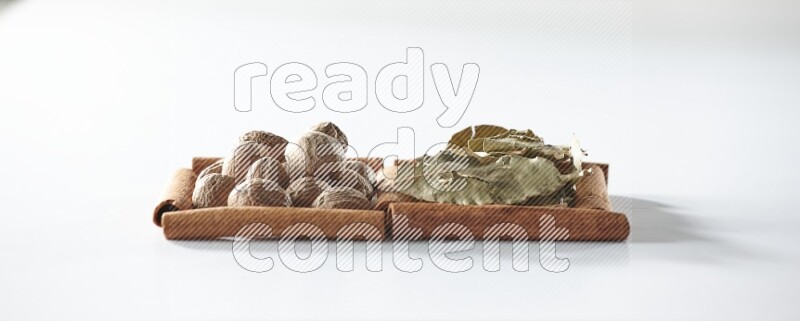 مربعان من أعواد القرفة ممتلئان بأوراق الغار وجوزة الطيب علي خلفية بيضاء