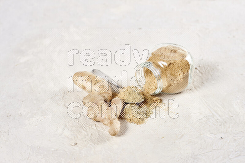 A glass jar full of ground ginger powder flipped with some spilling powder on white background