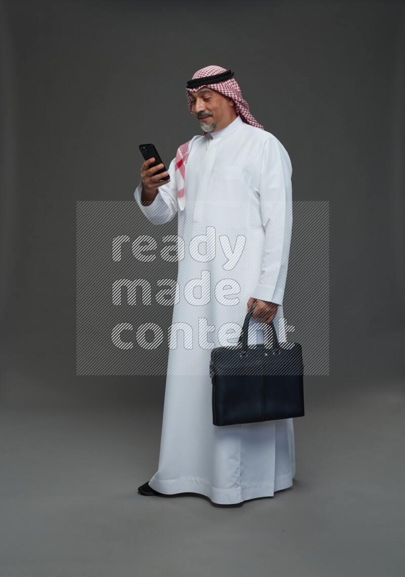 Saudi man with shomag Standing holding bag and phone on gray background