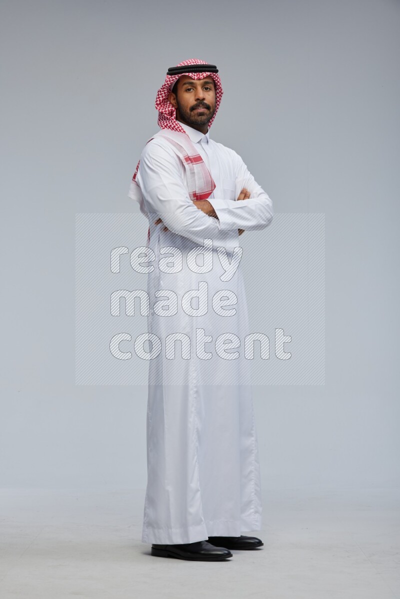 Saudi man Wearing Thob and shomag standing with crossed arms on Gray background