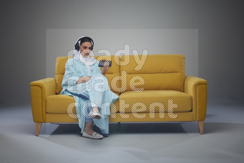 A Saudi woman sitting on a yellow Sofa Watching a Movie wearing Blue Abaya